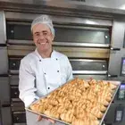 Chef Denilson Mattos, especialista em panificação artesanal e viennoiserie, vestindo dólmã branca de padeiro e apresentando uma fornada de pães.